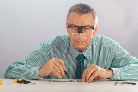 An older man wearing a shirt and tie, repairing a watch.