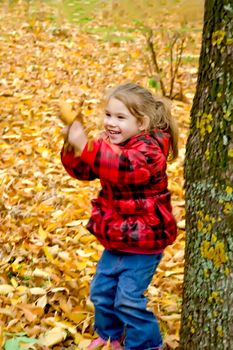 Little girl playing with leaves on a background of trees and yellow leaves