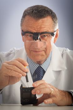 An older male wearing a white lab coat and repairing electronic equipments, like a technician or a repair man.