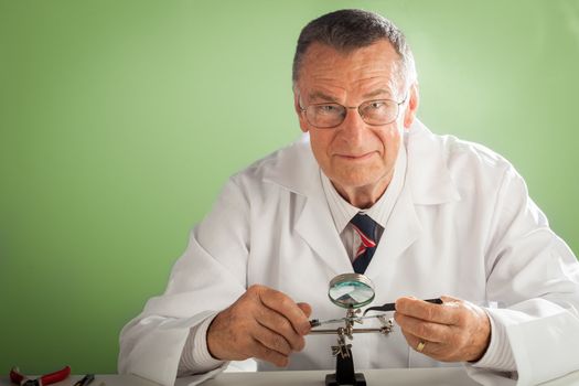 An older male wearing a white lab coat and repairing electronic equipments, like a technician or a repair man.