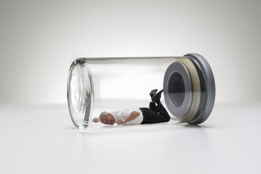 Conceptual studio image of a senior man trapped in a sealed glass jar lying on his stomach throwing a tantrum kicking his feet and beating his fists as he yells for his freedom