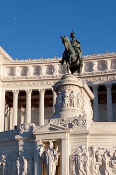 A dark equestrian statue in fron of white official building in Roma
