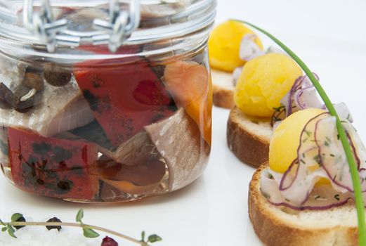 pickled herring in a glass jar with potato canapes