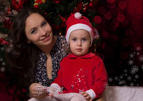 Mother and baby girl in Santa suit near Christmas tree