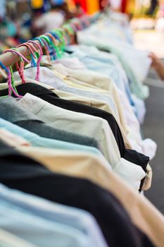 Old shirt hanging on plastic hangers in second hand maket