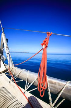 View of the bow of a sailing boat in calm blue sea with red rope riggings and white mast.