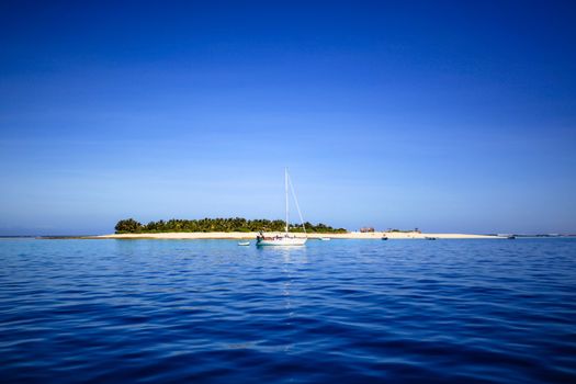 White sailing yacht in front of beautiful Fiji atoll island with white beach in the middle of the ocean.
