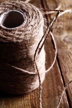 Artistic image of spool of thread and needle over wooden surface