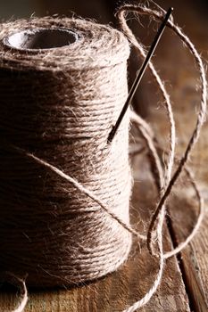 Artistic image of spool of thread and needle over wooden surface