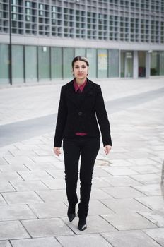 smiling business girl walking in front of a modern building