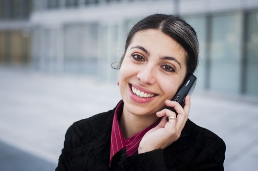 smiling business girl on the phone in front of a modern building