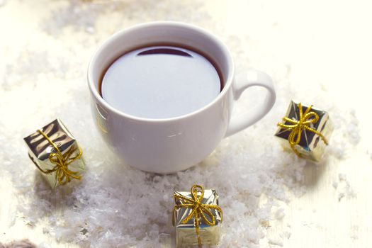 White cup of tea is in the snow near the gifts