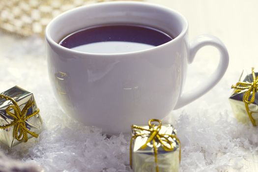 White cup of tea is in the snow near the gifts