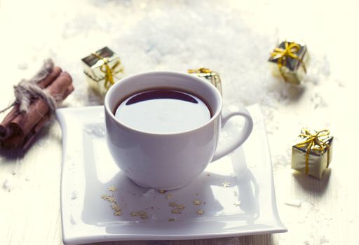 White cup of tea is in the snow near the gifts