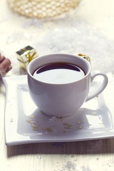 White cup of tea is in the snow near the gifts