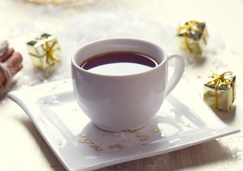 White cup of tea is in the snow near the gifts