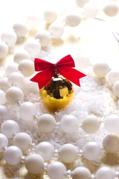 Golden ball with a red bow lying in the snow and beads