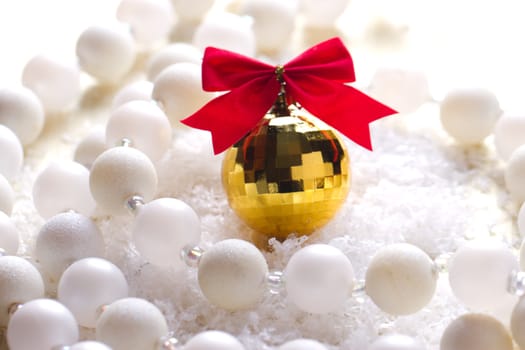 Golden ball with a red bow lying in the snow and beads