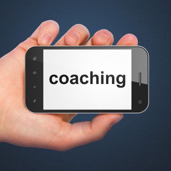 Hand holding smartphone with word coaching on display. Generic mobile smart phone in hand on dark blue background.