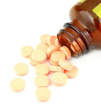 pills of vitamin C spilled out open container on white background