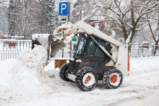 small excavator bobcat working on the street, cleaning snow