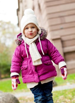 cute little child in pink jacket and hat outdoor in autumn having fun