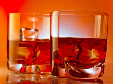 Two glasses of whiskey on the rocks over red background