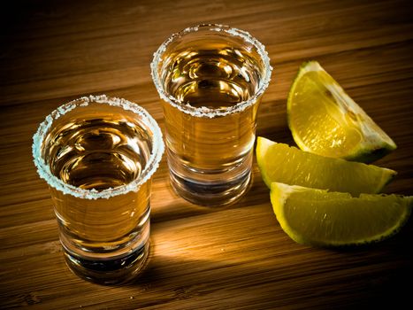 Two shot glasses of tequila with a rim of salt, and lime wedges