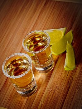 Two tequila shots with salt rims and lime wedges