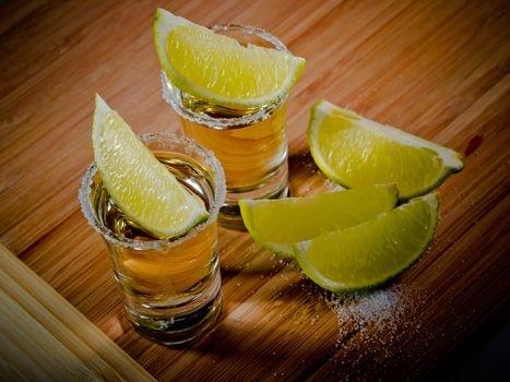 Two tequila shots with salt rims and lime wedges