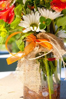 White, orange, and green wedding flower arrangements with burlap as the centerpieces for table settings at an outdoor reception.