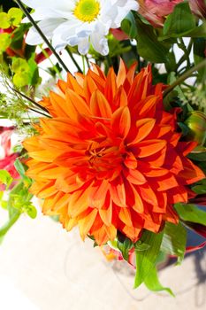 White, orange, and green wedding flower arrangements with burlap as the centerpieces for table settings at an outdoor reception.