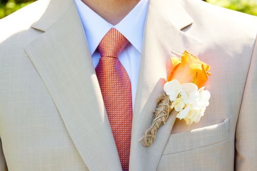 A groom in a light-colored suit is ready for his wedding day in formal attire with a boutineer on his jacket lapel.