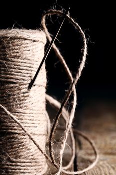 Artistic image of spool of thread and needle over wooden surface