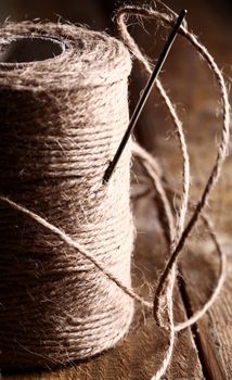 Artistic image of spool of thread and needle over wooden surface