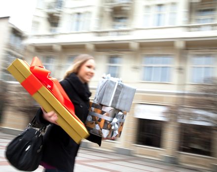 Motion blured, runing smiling female on the street carrying christmas gifts.