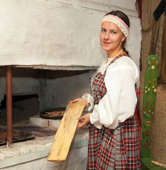 Girl in national costume prepares food on the stove. Russia. North