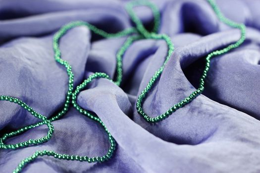 A close up view of the folds and details of shiny violet silk fabric with green beads