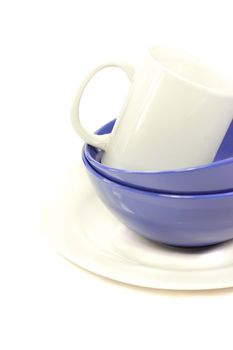 Ceramic white plate, two dark blue bowls and white mug on a white background