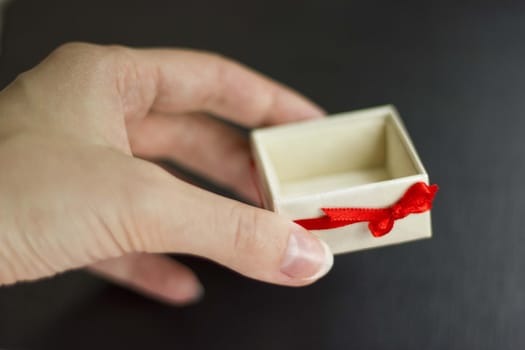 A woman hand holding a white gift box with red ribbon. Black background