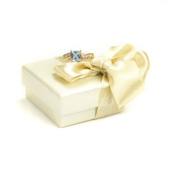 Closeup of golden ring with topaz and fair gift box with bow on a white background