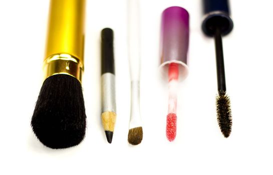 Close-up of eyeliner, applicator for lip gloss and brushes for eye-shadows, brusher and mascara on a white background