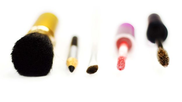 Close-up of eyeliner, applicator for lip gloss and brushes for eye-shadows, brusher and mascara on a white background