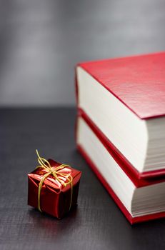 Close up of side view of two red books and small red present on a black background