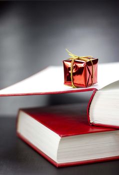 Close up of side view of two red books and small red present lying on them. Black background