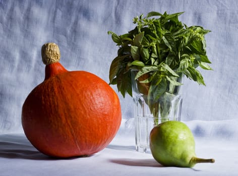 Still life of pumpkin, basil, pear on a colorful fabric background