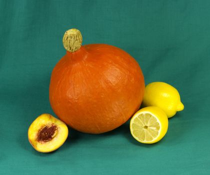 Still life of pumpkin, lemons and peach on a green fabric background