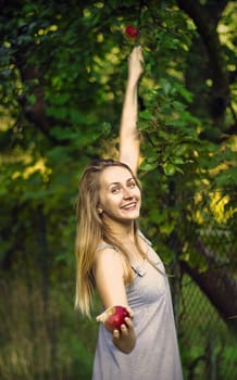 Smiling blond young woman holding an apple in a garden