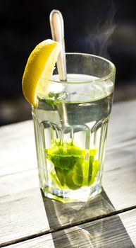 Glass of hot tea with a fresh peppermint and lemon, wooden background