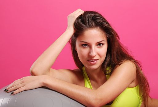 Close up of happy and beautiful woman with fitness ball isolated on a pink